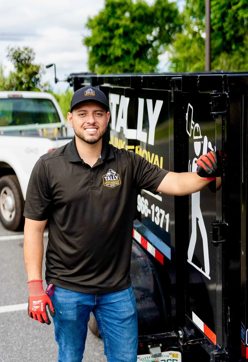 Owner of Tally Junk Removal and Demolition in a branded shirt standing beside the black dump trailer
