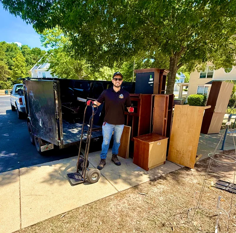 Dressers, cabinets, and a desk lined up beside the Tally Junk Removal dump trailer with a hand truck ready for loading